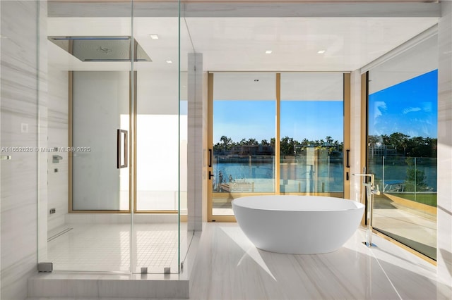 bathroom featuring tile patterned floors, a bathtub, a water view, and a wall of windows