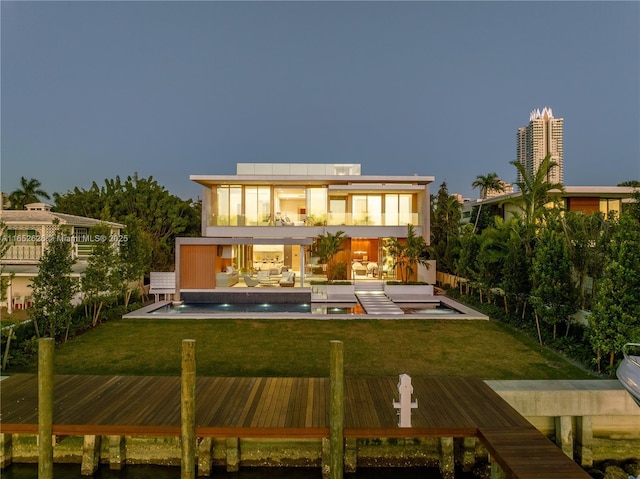 back house at dusk with a pool with hot tub, a patio area, a balcony, and a yard