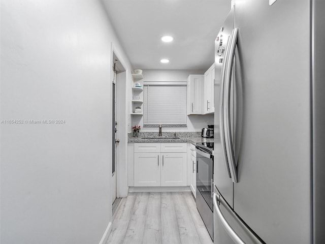 kitchen featuring light wood-type flooring, appliances with stainless steel finishes, stone countertops, white cabinetry, and sink