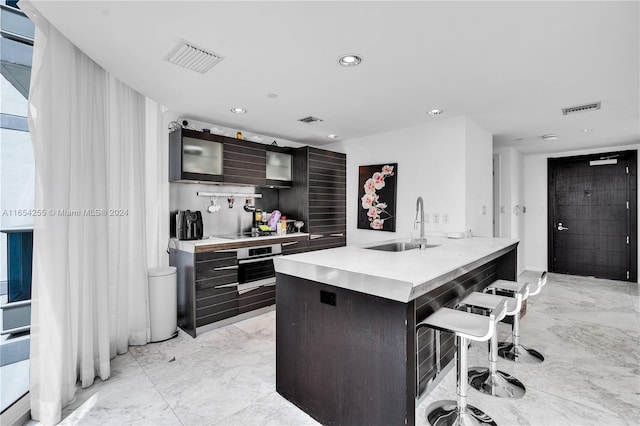 kitchen featuring oven, an island with sink, a breakfast bar, black stovetop, and sink