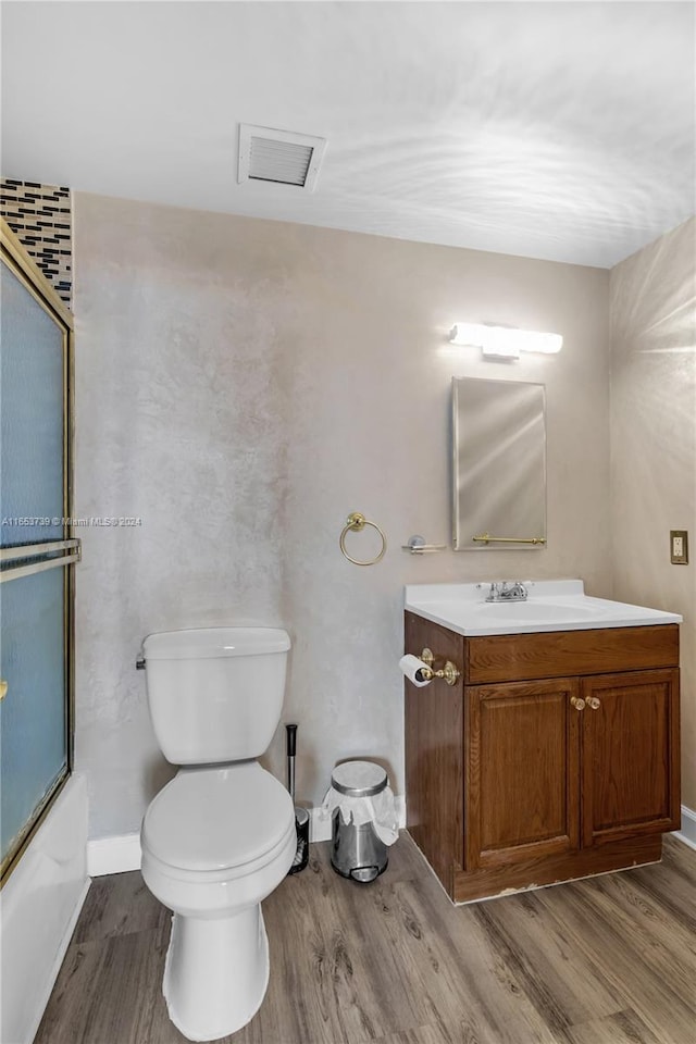 full bathroom featuring hardwood / wood-style floors, toilet, combined bath / shower with glass door, and vanity