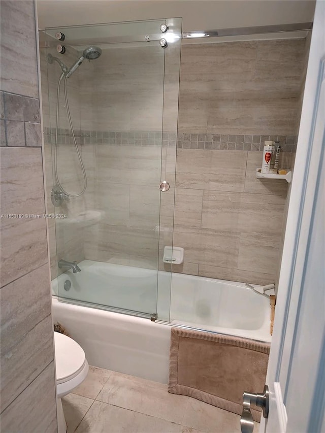 bathroom with tile patterned flooring, toilet, and combined bath / shower with glass door