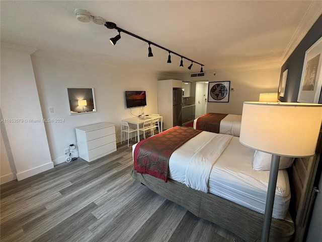 bedroom with crown molding, track lighting, hardwood / wood-style floors, and black fridge