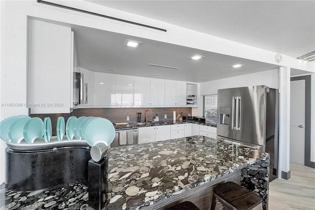 kitchen featuring white cabinets, backsplash, light wood-type flooring, high end refrigerator, and dark stone counters