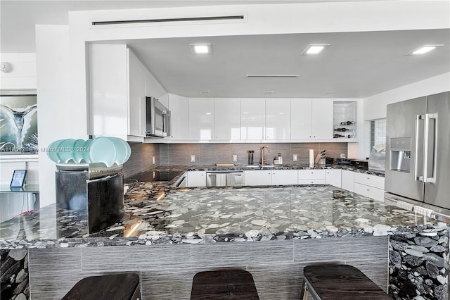 kitchen with tasteful backsplash, dark stone countertops, a kitchen bar, and kitchen peninsula