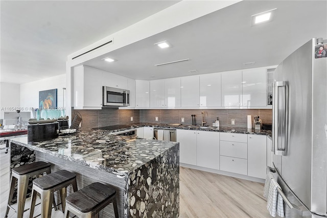 kitchen with dark stone countertops, backsplash, stainless steel appliances, kitchen peninsula, and light hardwood / wood-style floors