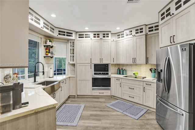 kitchen featuring sink, stainless steel appliances, tasteful backsplash, light stone counters, and light hardwood / wood-style floors