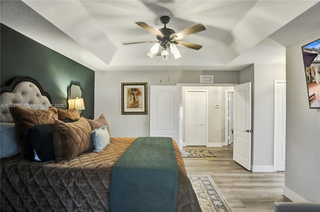 bedroom with a tray ceiling, ceiling fan, and light wood-type flooring