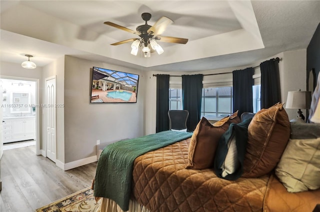 bedroom featuring a tray ceiling, wood-type flooring, ceiling fan, and ensuite bathroom