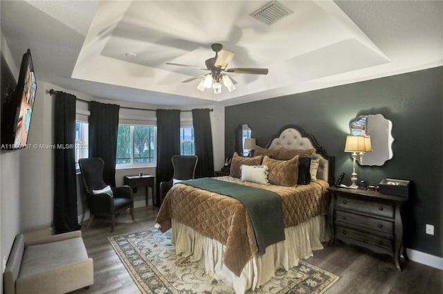 bedroom featuring dark hardwood / wood-style flooring, a tray ceiling, and ceiling fan