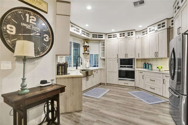 kitchen with appliances with stainless steel finishes, sink, light wood-type flooring, and decorative backsplash