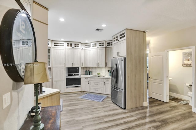 kitchen featuring backsplash, light hardwood / wood-style flooring, white cabinets, and appliances with stainless steel finishes