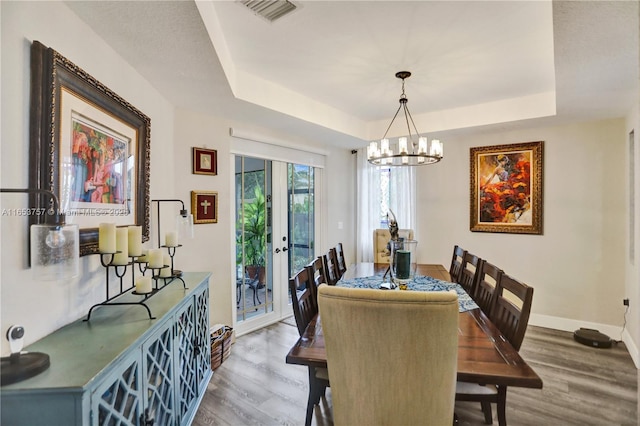 dining space with wood-type flooring, a tray ceiling, and a notable chandelier