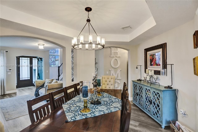 dining room with wood-type flooring, a raised ceiling, and a notable chandelier