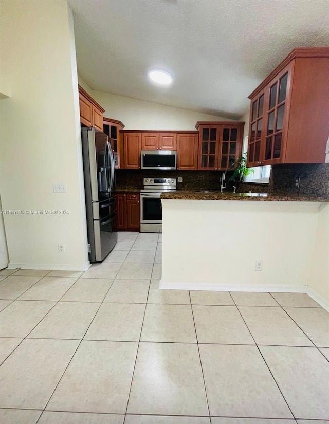 kitchen featuring lofted ceiling, stainless steel appliances, backsplash, dark stone counters, and light tile patterned floors