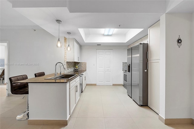 kitchen with stainless steel fridge, a raised ceiling, dark countertops, a sink, and backsplash