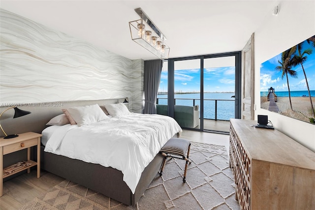 bedroom with a water view, access to exterior, floor to ceiling windows, and hardwood / wood-style flooring