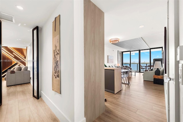 hallway with a wall of windows, light wood-type flooring, and a water view