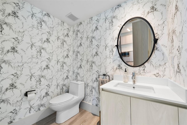 bathroom featuring visible vents, toilet, wood finished floors, wallpapered walls, and vanity