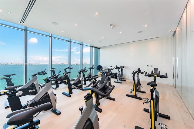 workout area featuring light wood-type flooring, a water view, and expansive windows