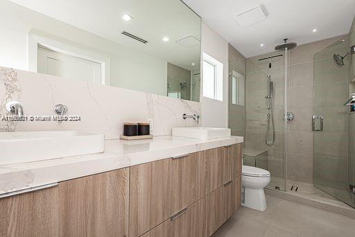 bathroom featuring vanity, toilet, walk in shower, and backsplash