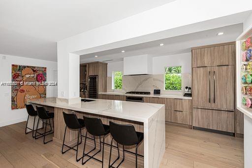 kitchen featuring a breakfast bar, built in fridge, backsplash, and light hardwood / wood-style floors