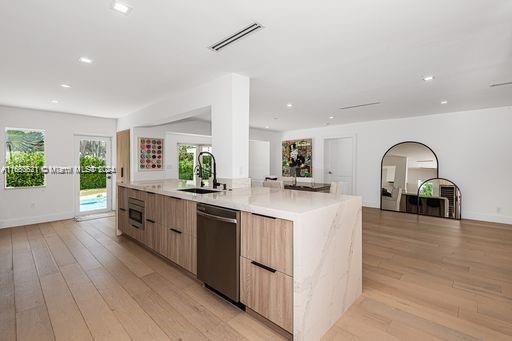 kitchen featuring stainless steel dishwasher, light hardwood / wood-style floors, a kitchen island with sink, and sink