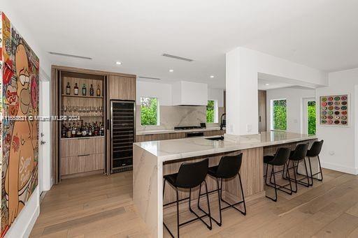 kitchen with white cabinetry, light hardwood / wood-style flooring, a kitchen bar, beverage cooler, and light stone countertops