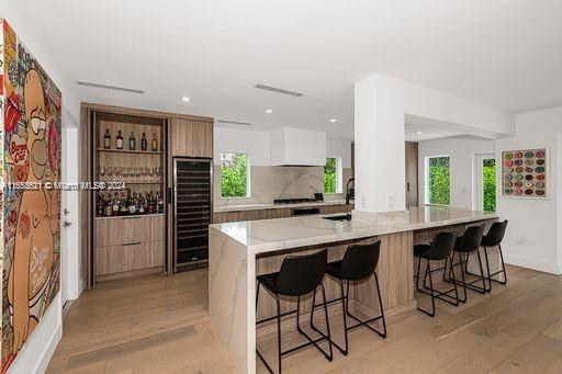 5231 SW 65th Ave, South Miami, FL 33155 - kitchen with modern cabinets, beverage cooler, light wood-type flooring, a kitchen breakfast bar, and recessed lighting