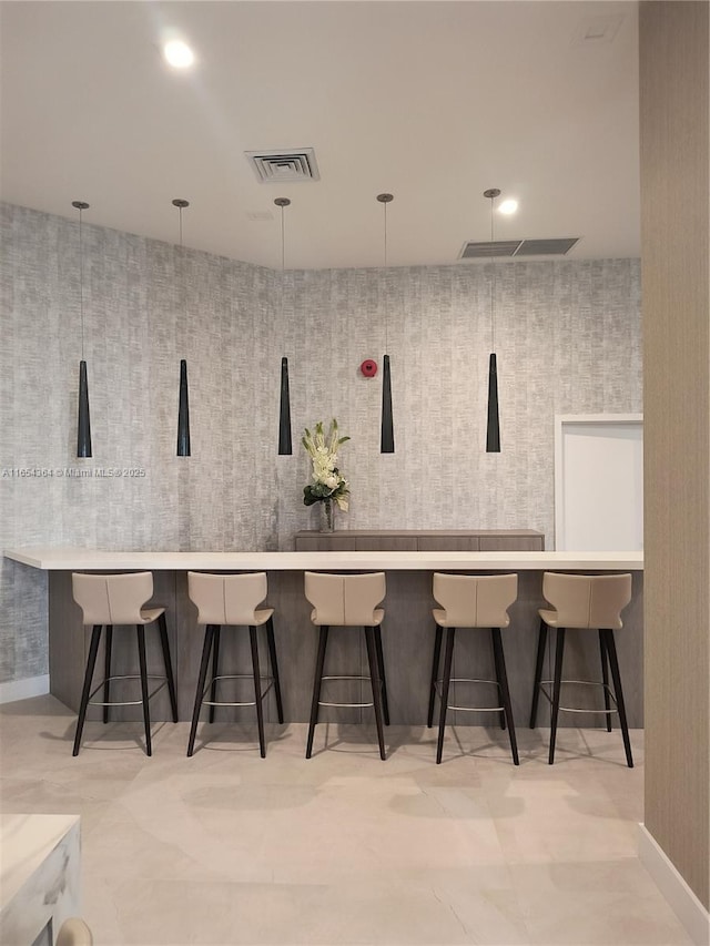 interior space with a breakfast bar area, light countertops, visible vents, hanging light fixtures, and wallpapered walls