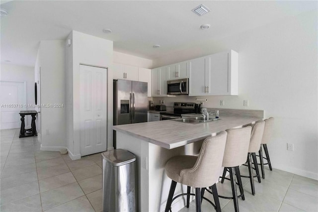 kitchen with a kitchen breakfast bar, appliances with stainless steel finishes, kitchen peninsula, sink, and white cabinetry