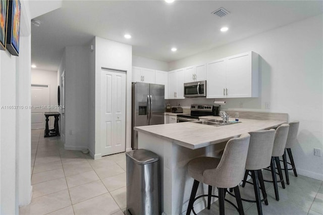 kitchen featuring white cabinetry, stainless steel appliances, a kitchen breakfast bar, kitchen peninsula, and sink