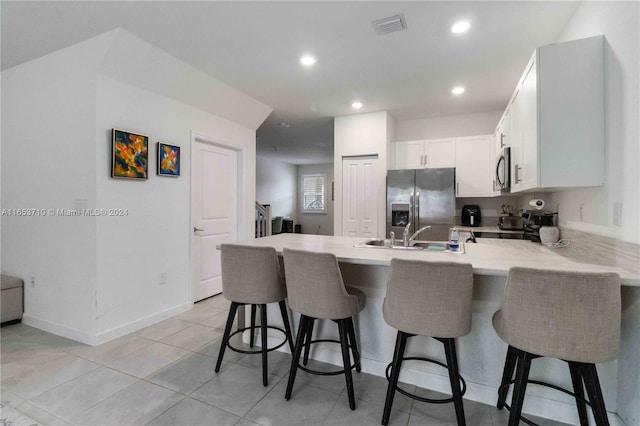 kitchen featuring appliances with stainless steel finishes, white cabinetry, sink, kitchen peninsula, and a breakfast bar