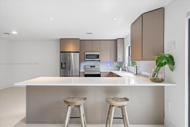 kitchen with appliances with stainless steel finishes, a kitchen breakfast bar, kitchen peninsula, and sink