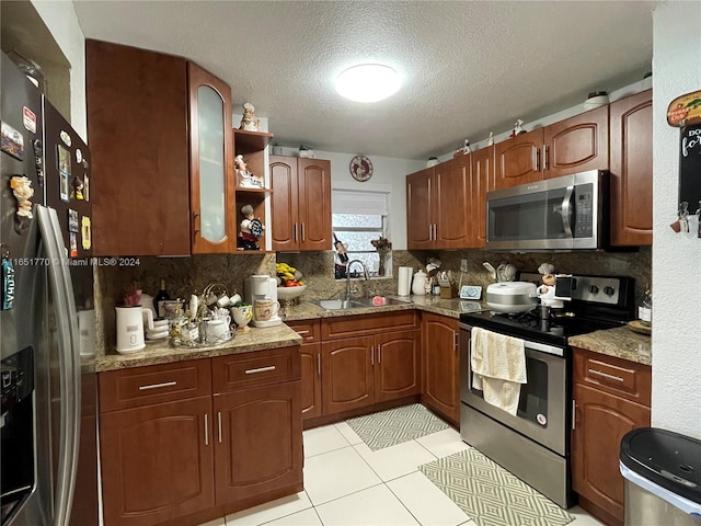 kitchen with light stone counters, sink, light tile patterned flooring, appliances with stainless steel finishes, and a textured ceiling