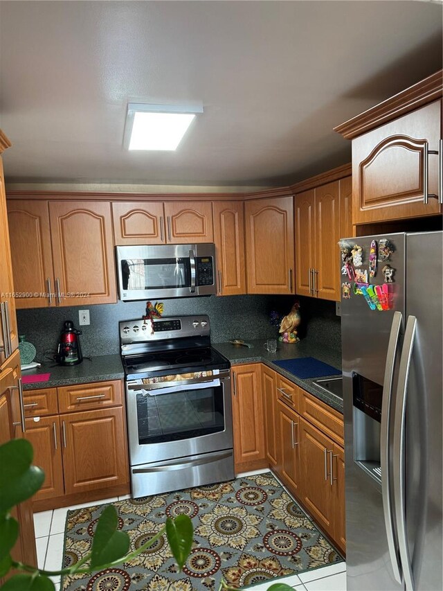 kitchen with dark stone counters, stainless steel appliances, and light tile patterned flooring