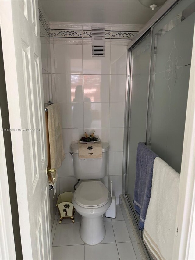 bathroom with tile patterned floors, a shower with shower door, toilet, and tile walls