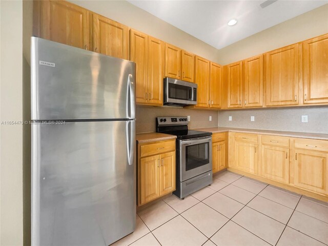 kitchen with light brown cabinetry, light tile patterned floors, and stainless steel appliances