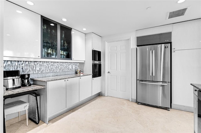 kitchen featuring decorative backsplash, white cabinets, light stone countertops, and built in fridge