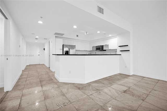 kitchen with appliances with stainless steel finishes, kitchen peninsula, and white cabinetry