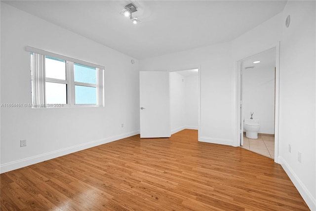 unfurnished bedroom with ensuite bathroom and light hardwood / wood-style floors