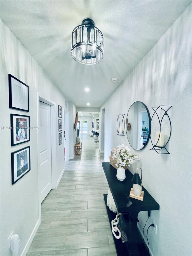 corridor with a chandelier, a textured ceiling, and light hardwood / wood-style flooring