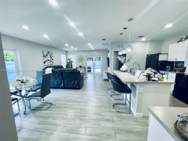 kitchen with white cabinetry, black appliances, a kitchen breakfast bar, a center island, and pendant lighting