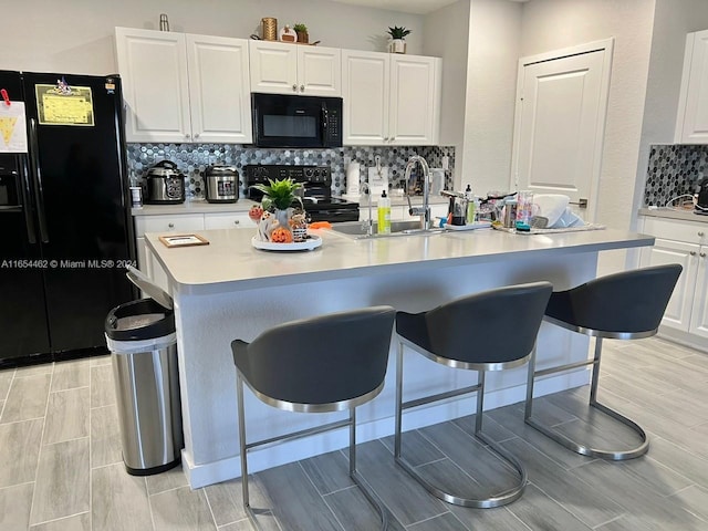 kitchen with black appliances, tasteful backsplash, white cabinetry, a breakfast bar area, and a kitchen island with sink