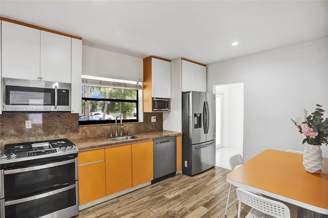 kitchen with light hardwood / wood-style flooring, stainless steel appliances, white cabinetry, sink, and decorative backsplash