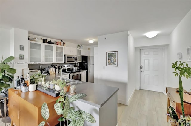 kitchen with appliances with stainless steel finishes, kitchen peninsula, sink, white cabinetry, and light wood-type flooring