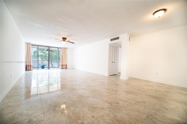 empty room featuring visible vents, a ceiling fan, expansive windows, a textured ceiling, and baseboards