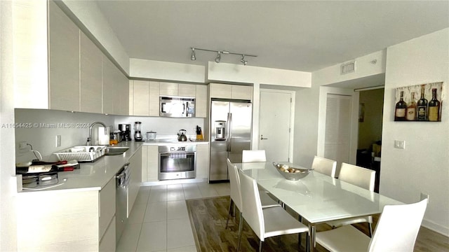 kitchen featuring sink, appliances with stainless steel finishes, track lighting, and light tile patterned flooring