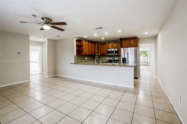 kitchen featuring appliances with stainless steel finishes, light stone countertops, kitchen peninsula, ceiling fan, and decorative backsplash