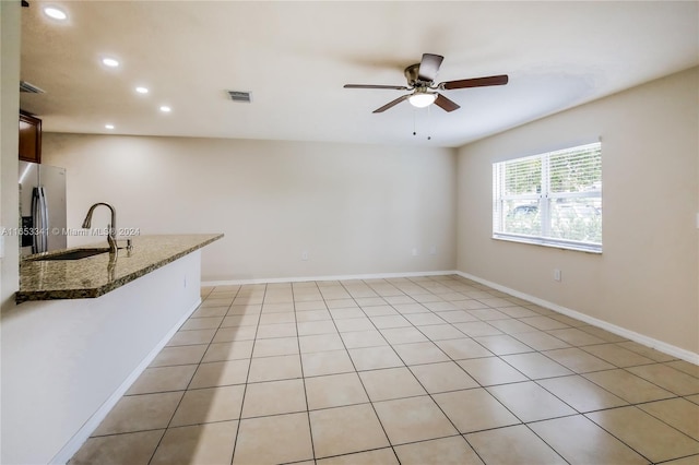 interior space featuring dark stone countertops, stainless steel fridge, light tile patterned floors, sink, and ceiling fan